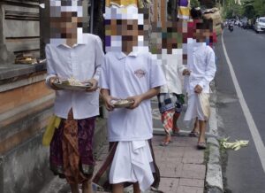 白い正装をした子どもたちが、供物を手に持ってウブドの通りを歩いている様子。