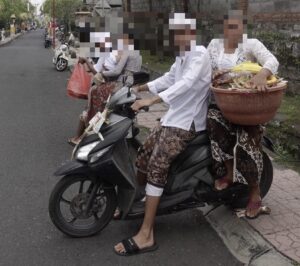 クニンガンの朝、正装した親子が供物を持ち、バイクで寺院へ向かっている様子。