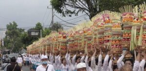 ウブドの通りで、正装した人々が供物や傘を持ち、寺院へ向かって行列で歩いている様子。