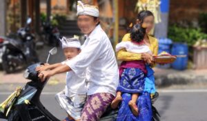バリ島ウブドの通りで、バイクに乗った男性と子ども、後ろに座る女性が笑顔でカメラに応じている様子。